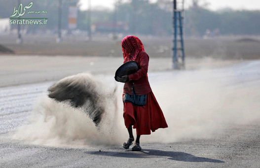 یک زن در حال پاشیدن ترکیبی از خاکستر، پودر بتن و سیمان پیش از آسفالت کردن یک جاده در احمدآباد هند