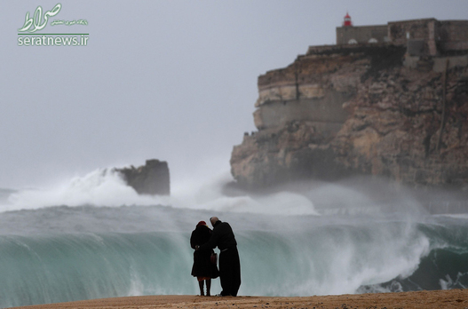 زن و شوهر ایستاده مقابل امواج بزرگ در نزدیکی قلعه سائو میگوئل آرکانجو پرتغال