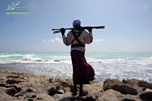 یک دزد دریایی مسلح ایستاده در امتداد خط ساحلی در سواحل شمال شرقی سومالی