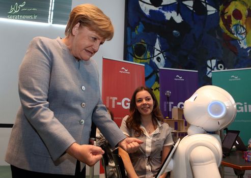 آنگلا مرکل صدراعظم آلمان با چهره درهم و مشت های گره کرده هنگام مواجه با یک ربات در برلین
