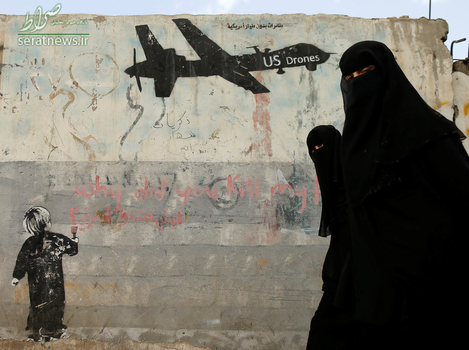 زنان یمنی در حال عبور از یک طرح گرافیتی روی دیوار در محکومیت حمله هواپیماهای بدون سرنشین آمریکا - صنعا، یمن