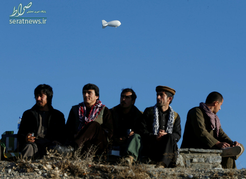 نشستن مردان افغان روی تپه ای در کابل برای استراحت و رد شدن یک بالون سفید رنگ امنیتی ناتو از آسمان